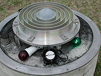 A close up of the antenna connected to the GODE and GODZ GNSS receivers. Two light bulbs (one red on left and one white in front) are installed under the radome; these bulbs serve two purposes: (1) to reduce the humidity levels within the radome and (2) to prevent the GSFC snow plow operators from running into the monument. Charcoal is scattered beneath the antenna to absorb moisture. A fan is also running under the dome to provide air circulation.